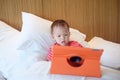 Little Asian 18 months, 1 year old baby boy child leaning against pillows on bed watching a video from tablet pc