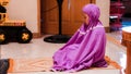 Little Asian Muslim girl in purple muslimah clothes is praying at home Royalty Free Stock Photo