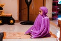 Little Asian Muslim girl in purple muslimah clothes is praying at home Royalty Free Stock Photo