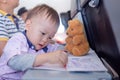 Little Asian 1 year old toddler boy coloring in coloring book with crayons during flight on airplane