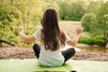 Little athletic girl sitting on sporty rug and practicing yoga in front of river. Active kid meditating in nature.