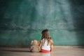 Little girl with teddy bear sitting on floor in empty room. Autism concept