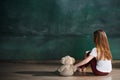 Little girl with teddy bear sitting on floor in empty room. Autism concept Royalty Free Stock Photo