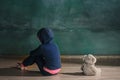 Little girl with teddy bear sitting on floor in empty room. Autism concept