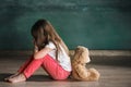 Little girl with teddy bear sitting on floor in empty room. Autism concept