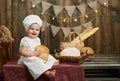 Little baby baker holding bread and wide smiling in a rustic interior