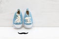 Little baby blue sneakers and mustaches on a white wooden background Royalty Free Stock Photo