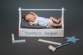 little baby in bodysuit crying while lying in wooden toolkit with daddys