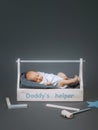 little baby in bodysuit lying in wooden toolkit with daddys helper lettering and hammer