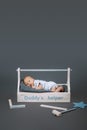little baby in bodysuit lying in wooden toolkit with daddys helper lettering and hammer