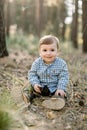 Little baby boy in checkered shirt, sitting in autumn pine forest, playing with cone and smiling to camera. Outdoor Royalty Free Stock Photo