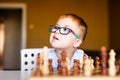 Little baby boy with down syndrome with big blue glasses playing chess in kindergarten