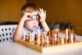 Little baby boy with down syndrome with big blue glasses playing chess in kindergarten Royalty Free Stock Photo