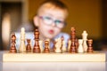 Little baby boy with down syndrome with big blue glasses playing chess in kindergarten Royalty Free Stock Photo