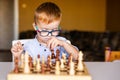 Little baby boy with down syndrome with big blue glasses playing chess in kindergarten Royalty Free Stock Photo