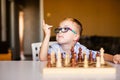 Little baby boy with down syndrome with big blue glasses playing chess in kindergarten Royalty Free Stock Photo