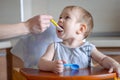 Little baby boy eats opening his mouth wide sitting on a chair in the kitchen. Mom feeds holding a spoon of porridge Royalty Free Stock Photo