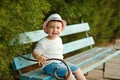 Little baby boy in a hat sitting on a bench and smiling in the s Royalty Free Stock Photo