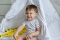 Little baby boy sitting in a tepee tent and funny wrinkles his n Royalty Free Stock Photo