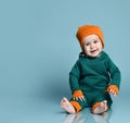 Little baby boy in stylish casual jumpsuit, cap and barefoot sitting on floor and smiling over blue wall background Royalty Free Stock Photo