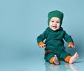 Little baby boy in stylish casual jumpsuit, cap and barefoot sitting on floor and smiling over blue wall background Royalty Free Stock Photo