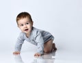 Little baby boy toddler in grey casual jumpsuit and barefoot crawling on floor, smiling and looking up over white wall background Royalty Free Stock Photo