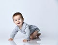 Little baby boy toddler in grey casual jumpsuit and barefoot crawling on floor, smiling and looking up over white wall background Royalty Free Stock Photo