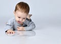 Little baby boy toddler in grey casual jumpsuit barefoot lying on floor and looking down at reflection over white wall background Royalty Free Stock Photo