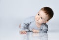 Little baby boy toddler in grey casual jumpsuit and barefoot lying on floor, smiling and looking up Royalty Free Stock Photo