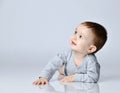 Little baby boy toddler in grey casual jumpsuit and barefoot lying on floor, smiling and looking up Royalty Free Stock Photo