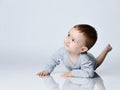 Little baby boy toddler in grey casual jumpsuit and barefoot lying on floor, smiling and looking up Royalty Free Stock Photo