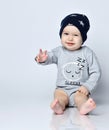 Little baby boy toddler in grey casual jumpsuit, black cap with stars and barefoot sitting on floor, smiling and gesticulating Royalty Free Stock Photo