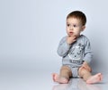 Little baby boy toddler in grey casual jumpsuit, cap and barefoot sitting on floor and feeling interested looking aside