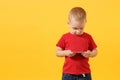 Little baby boy 3-4 years old in red t-shirt holding in hand, playing game on mobile phone isolated on yellow background Royalty Free Stock Photo