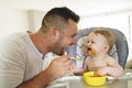 A Little baby eating her dinner and making a mess with dad on the side Royalty Free Stock Photo