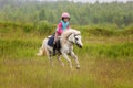 Little baby girl confident riding a horse at a gallop across the field