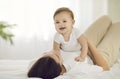 Little baby girl and her mom in morning having fun together playing on white bed.
