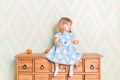 A little baby girl in her room sitting cross-legged on chest of drawers with tangerines on the rhomb wallpaper Royalty Free Stock Photo