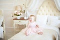 Smiling little baby girl in pink dress on the bed