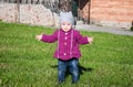 Little baby girl in jeans jacket and hat making learning to walk his first steps on the lawn in the green grass Royalty Free Stock Photo