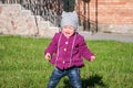 Little baby girl in jeans jacket and hat making learning to walk his first steps on the lawn in the green grass it has not very go Royalty Free Stock Photo