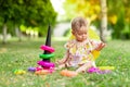 Little baby girl 7 months old sitting on the green grass in a yellow dress and hat and playing with a pyramid, early development Royalty Free Stock Photo