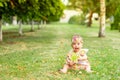 Little baby girl 7 months old sitting on a green lawn in a yellow dress and playing with a toy, walking in the fresh air, space Royalty Free Stock Photo