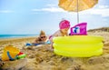 Baby girl plays yellow inflatable pool mom checks her sunbathing on beach towel Royalty Free Stock Photo