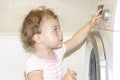 Little baby girl presses the buttons on the washing machine. European Caucasian child and washer