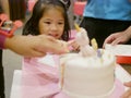 Little baby girl reaching her hand out to a birthday cake in front of her, as it is so irresistibly attracted to her