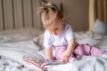 little baby girl reading, looking at pictures in book on bed at home, An inquisitive baby wants to read new fairy tale. Royalty Free Stock Photo