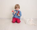 Little baby girl siting on the floor in bright room plays with cat and tulip flowers. Happy child playing at home Royalty Free Stock Photo