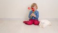 Little baby girl siting on the floor in bright room plays with cat and tulip flowers. Happy child playing at home Royalty Free Stock Photo