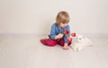 Little baby girl siting on the floor in bright room plays with cat and tulip flowers. Happy child playing at home Royalty Free Stock Photo